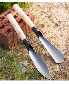 Macro view of carbon steel garden trowels with wooden handles on outdoor soil ground