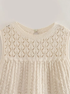 Dettaglio del top in maglia traforata con trama all'uncinetto e bottone a perla sul retro