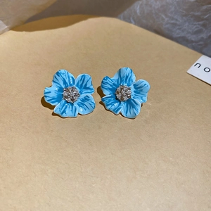 Vue macro de boucles d'oreilles fleurs en émail bleu avec perle centrale sur fond neutre