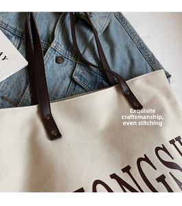Close-up of canvas tote bag with brown leather handles and reinforced metal rivets
