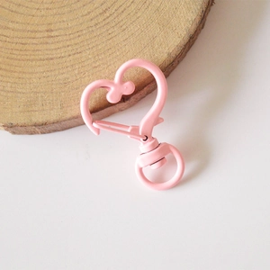 Pink heart-shaped metal lobster clasp keychain accessory on a wooden aesthetic background