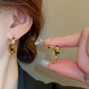 Macro detail of a gold drop earring featuring a brown teardrop stone on model's ear