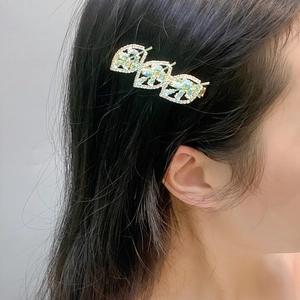 Close-up of golden leaf hair clip with green gems and crystals worn on hair