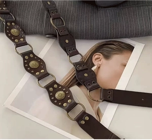 Close-up of dark brown vintage leather belt with brass rings and sunburst rivets