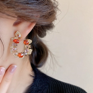 Detail of C-shaped drop earrings with colorful zircon stones worn by a model