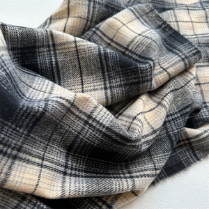 Close-up of soft beige and black plaid cashmere-like fabric texture with a fuzzy finish
