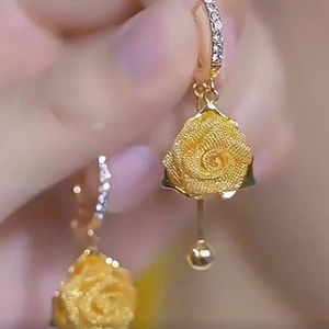 Close-up of golden rose pendant earrings with frosted petals and zircon accents