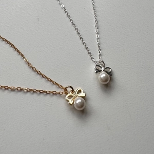 Detail of elegant gold and silver bow necklaces with single pearls on a minimalist background