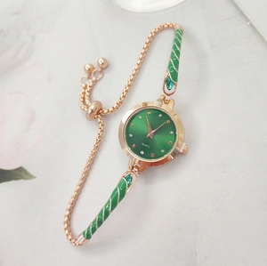 Detail of green quartz watch and gold adjustable bracelet set on white marble background