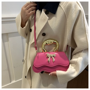 Detail of pink crossbody bag with golden metal handle and bow decoration on model