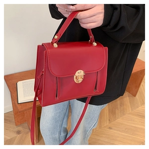 Detail of red leather crossbody bag with golden turn-lock and metallic zippers
