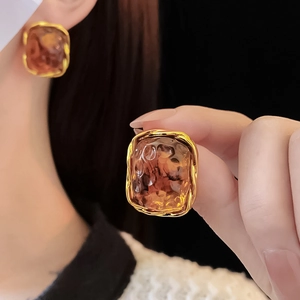Detail of square amber resin earring with gold twisted metal frame on ear lobe