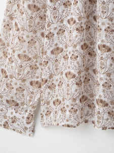 Gros plan sur le tissu en mousseline fleurie avec motifs dorés et ourlet à volants