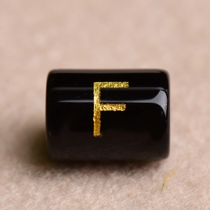Macro shot of a black cylindrical bead featuring a gold-stamped letter F for DIY jewelry