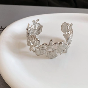 Detailed close-up of textured silver starfish and seashell elements on the open cuff bracelet