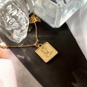Macro detail of gold square rose pendant necklace against a dark textured background