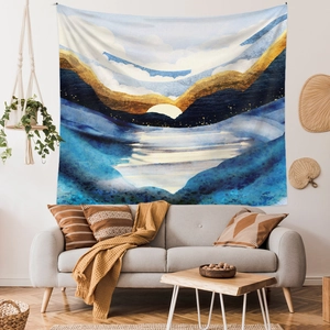Modern abstract wall tapestry featuring golden sun and blue mountains in a cozy living room