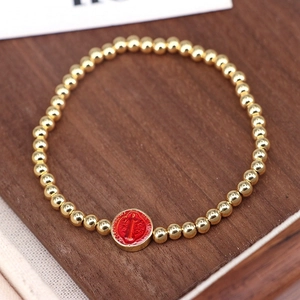 Close-up of golden beaded bracelet featuring a red St. Benedict religious medal charm