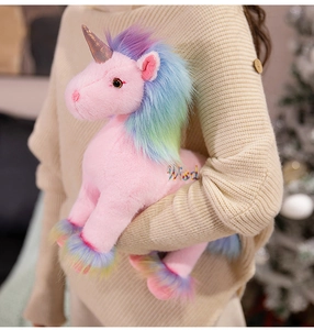 Detail of pink unicorn plush toy with rainbow mane and 'Wish' embroidery in a cozy setting