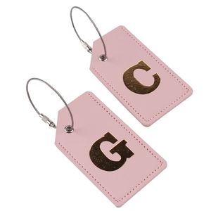Detail of two pink PU leather luggage tags with gold metal letters C and G