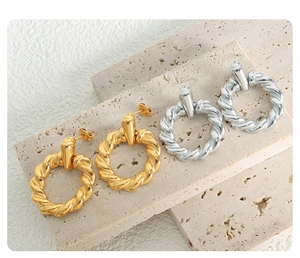 Detailed view of twisted rope earrings in gold and silver finishes on textured stone