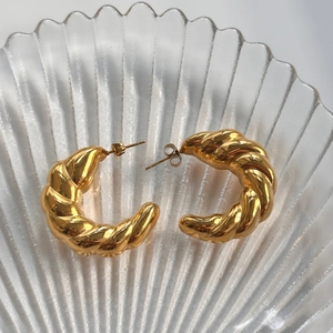 Detailed view of chunky twisted golden C-shape earrings on a glass decorative plate