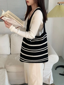 Close-up of minimalist black and white striped knit tote bag held by a model indoors