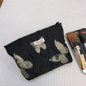 Detail der schwarzen Kosmetiktasche mit goldener Schmetterlingsstickerei und Reißverschluss