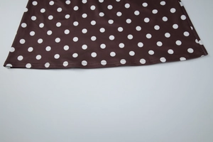 Gros plan de l'ourlet à double surpiqûre et motifs à pois blancs sur tissu brun