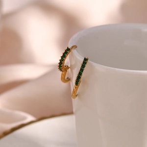 Detail of 18K gold earrings with green zircon gems hanging on a white ceramic cup