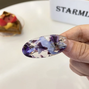 Detail of oval acetate hair clip with purple marble texture and gold lettering