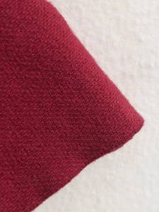 Nahaufnahme von dunkelrotem Strickstoff mit detaillierter Textur und hochwertigen Fasern