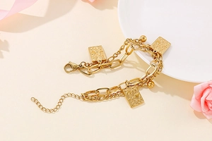 Detail of layered gold bracelet featuring poker card pendant and polished metal beads