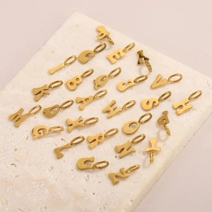 Golden stainless steel alphabet pendants set on marble surface for DIY jewelry making