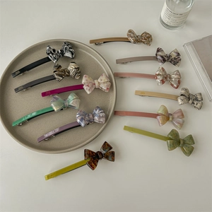 Minimalist acetate bow hair clips in multiple colors displayed on a beige ceramic plate