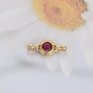 Macro shot of a golden jewelry clasp featuring a round red gemstone inlay on white fabric