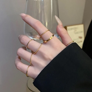 Stackable set of gold minimalist band rings worn by model holding a glass cup