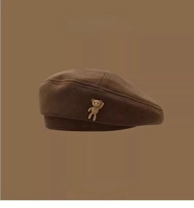 Detail of dark brown wool beret with a small beige 3D teddy bear decorative patch