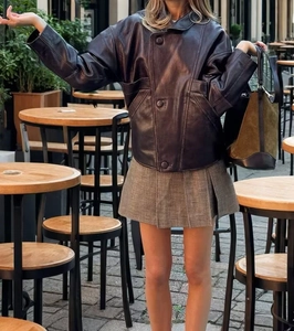 Gros plan d'une veste rétro en cuir associée à une jupe plissée à carreaux style urbain