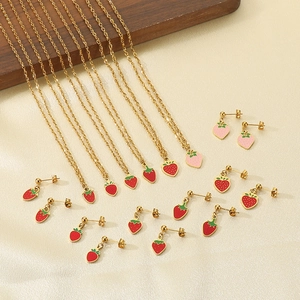 Detailed close-up of golden strawberry enamel pendants on steel necklaces and earrings