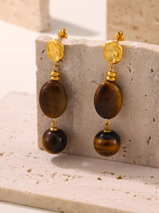 Macro shot of tiger eye stone earrings on beige rock stand with 18k gold plating details