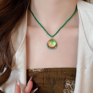 Detail of vintage beaded necklace with green crystals and a round resin pendant