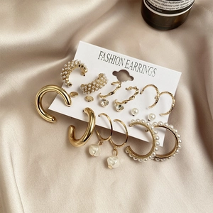 9-piece gold hoop earring set with pearls and twisted metal on beige silk background
