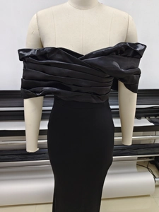Detail of the pleated off-shoulder neckline on a black evening gown with satin finish