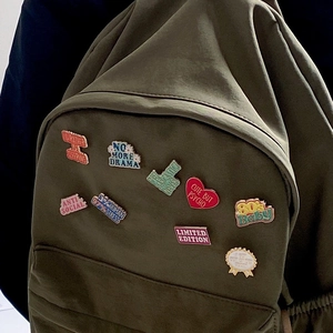 Détail de pin's créatifs en émail avec citations drôles sur un sac à dos vert