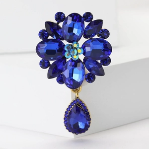Detailed view of blue crystal flower brooch with a teardrop pendant on white base