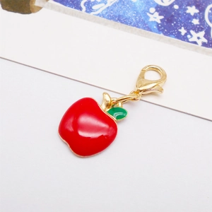 Macro detail of a red apple charm with gold lobster clasp and green leaf for DIY bags