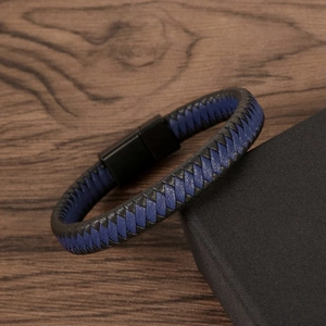 Close-up of dual-tone braided leather bracelet with black magnetic clasp on textured box
