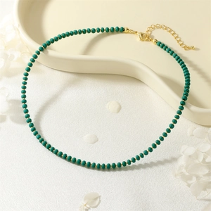 Detail of emerald green beaded necklace with gold clasp on white ceramic tray