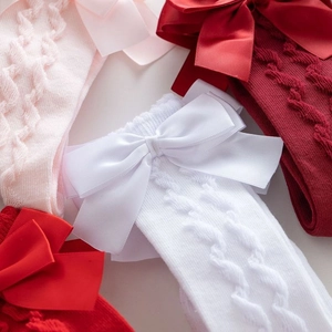Detailed view of knitted cotton baby socks with large satin bows in pink, red and white